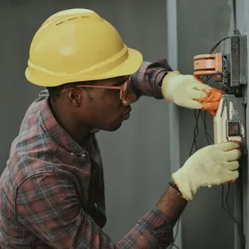 Électricien portant un casque de sécurité, au travail sur un panneau électrique