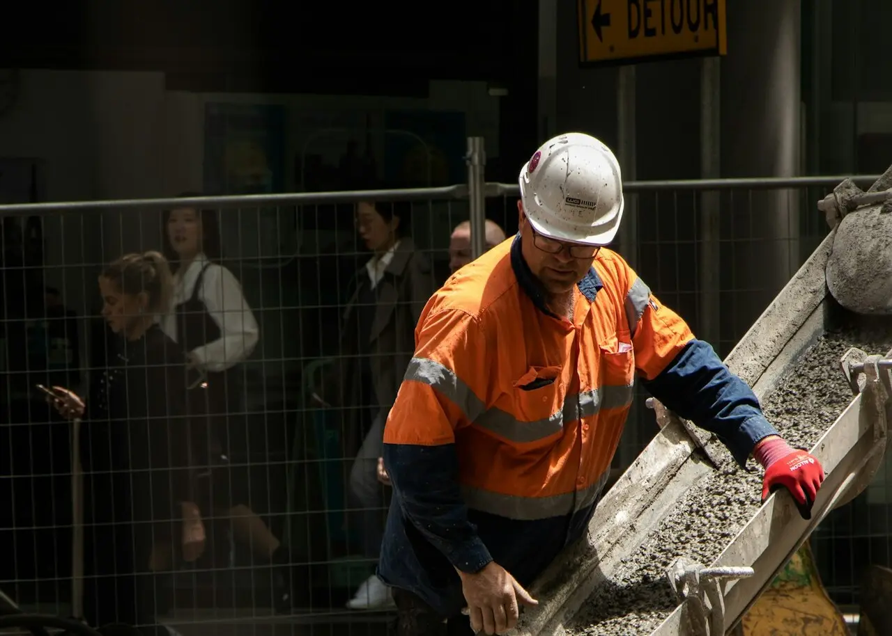 Travailleur en casque et dossard qui dirige une coulée de béton sur un chantier
