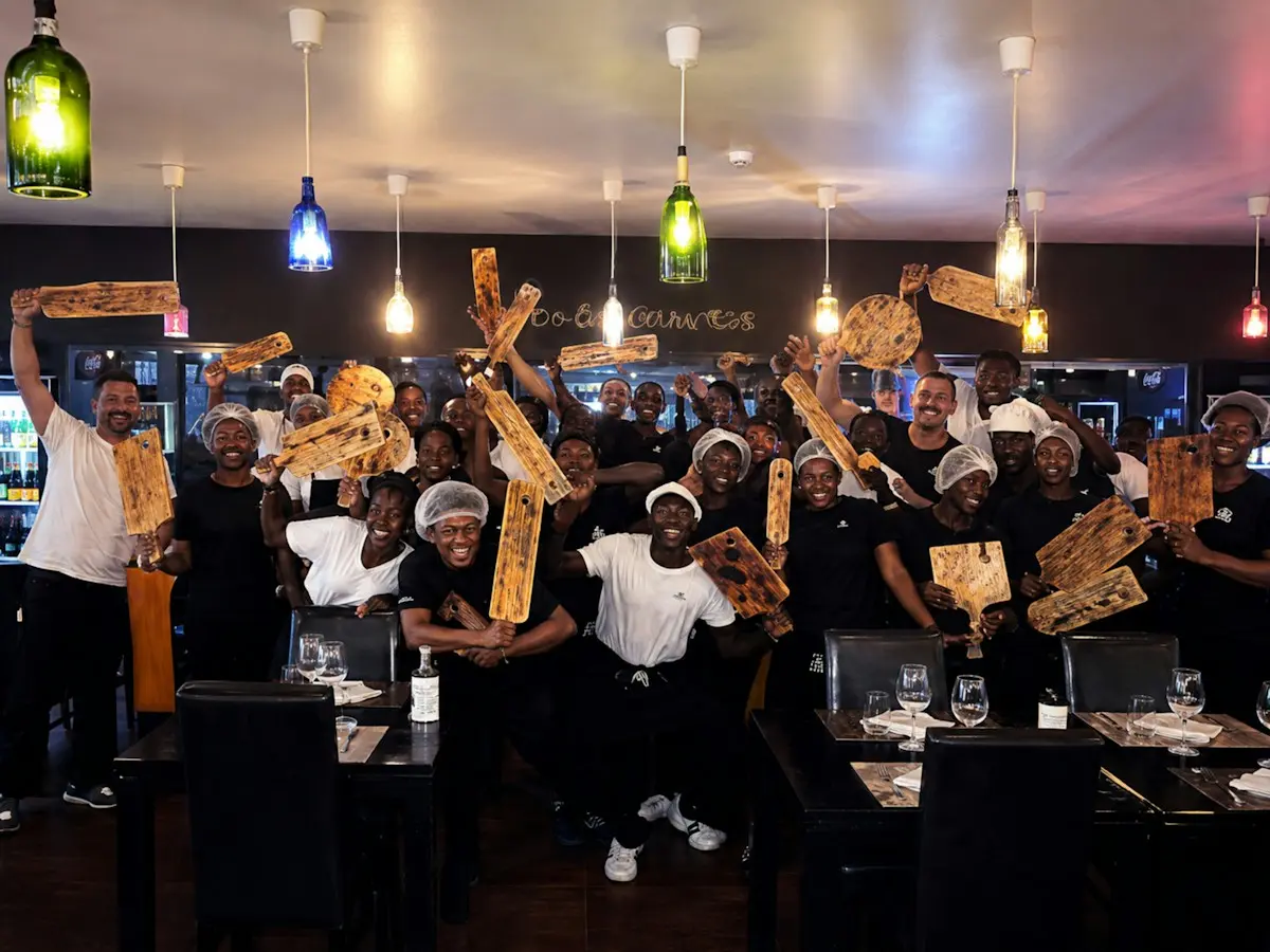 Toute l'équipe d'un restaurant, réunie en salle, brandit ses planches de service en souriant